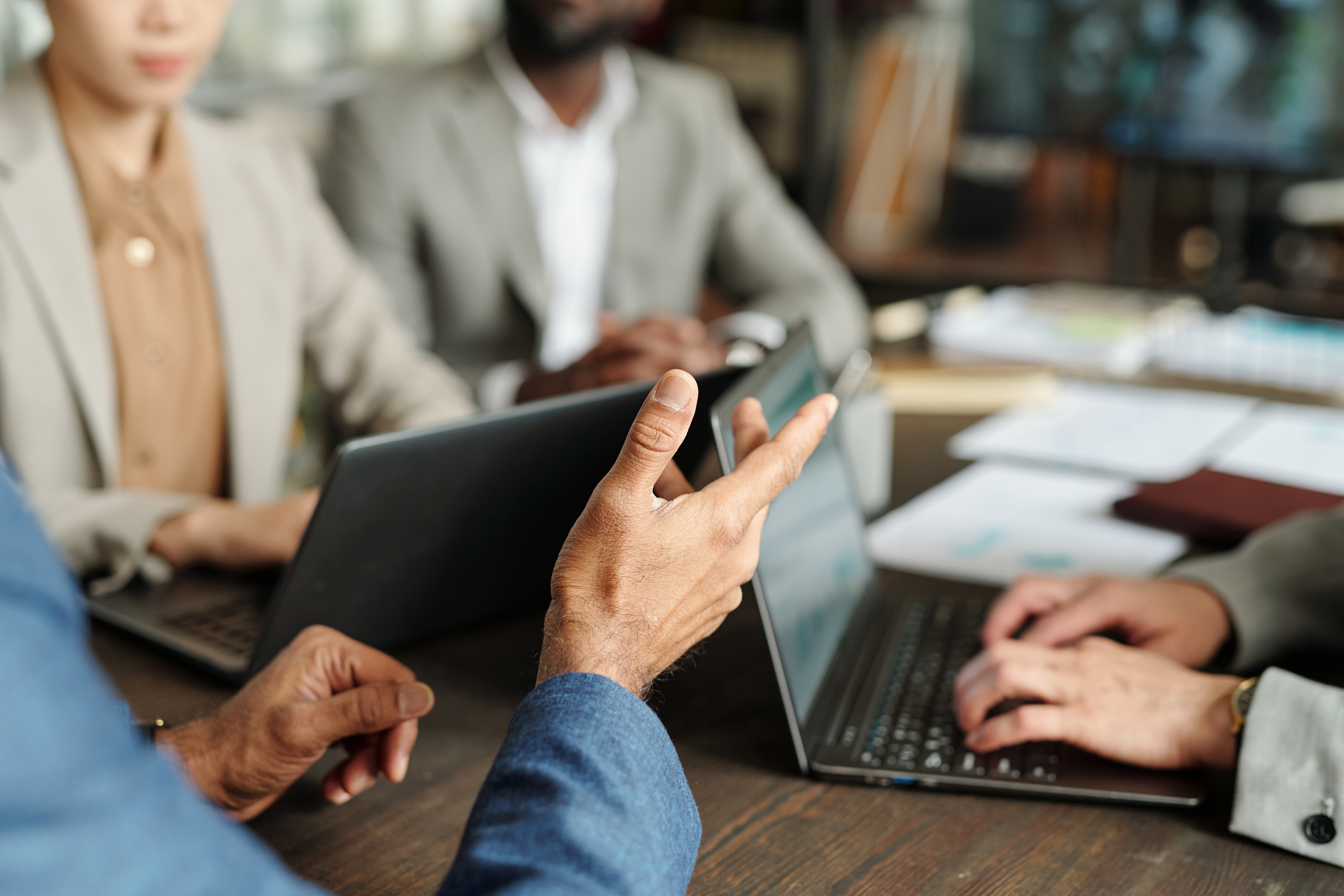 Multiethnic Group of Business Professionals Collaborating during Meeting Multiethnic group of middle aged professionals collaborating around laptops during business meeting, hands gesturing while discussing project, focus on teamwork and communication